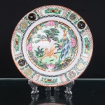 Prato executado em porcelana chinesa, decoração policromada e dourada executada em esmaltes sobre o vidrado, ao gosto da Família Rosa. Reserva central delimitada por cartela lobulada, contendo composição com tigre e ave de rapina, entre pinheiro, formações rochosas, flores e vegetação. Aba ornamentada por painéis alternados com frutos e motivos florais, intercalados por medalhões circulares contendo caracteres auspiciosos, além de frisos geométricos em vermelho-ferro e negro. Contorno realçado por filete alaranjado. No reverso, marca quadrangular em vermelho-ferro com quatro caracteres chineses(Huali Chang Zao).  Medida: Diam.: 21cm.