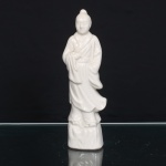 Escultura executada em porcelana branca moldada e esmaltada, representando Han Xiangzi, um dos Oito Imortais(Baxian) da tradição taoista. Personagem juvenil em posição ereta, cabelos reunidos em coque, trajando túnica de mangas amplas e panejamento sobreposto, com mãos dispostas diante do torso. Assente sobre pedestal modelado à maneira de formação rochosa. Corpo oco com abertura de queima. Produção chinesa do século XX, segundo a tradição das porcelanas de Dehua, Fujian, conhecidas no Ocidente como Blanc de Chine. Medidas: Alt.: 22 x Comp.: 6,5 x Larg.: 5 cm