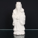 Escultura executada em porcelana representando Lu Xing, divindade associada à prosperidade e posição social, integrante da tríade Fu Lu Shou. Apresenta-se de pé, com longa barba, toucado de dignitário e indumentária talar de amplas mangas, portando ruyi, atributo ligado à autoridade e à realização dos desejos. Corpo oco, com abertura de queima na base. Produção chinesa do século XX, segundo a tradição das porcelanas brancas de Dehua, Fujian, conhecidas no Ocidente como Blanc de Chine. Medidas: Alt.: 28,5 x Comp.: 12 x Larg.: 9cm