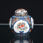 Pote com tampa em porcelana chinesa de corpo globular, com tampa abobadada. Decoração policroma sob esmalte, organizada em reservas delimitadas por volutas azuis, contendo composições de frutos, flores e folhagens; campos intermediários preenchidos por motivos florais e borboletas sobre fundo dourado, com faixas ornamentais em azul junto ao ombro e à base. Tampa com ornamentação floral e friso dourado. Na base, marca de manufatura Ling Nan, acompanhada das inscrições em caracteres chineses(Zhongguo zhizao - Fabricado na China) e Made in China. Medidas: Alt.: 9 x Diam.: 9cm.
