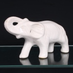 Escultura de elefante em cerâmica esmaltada branca, modelagem oca, representado em marcha, com tromba elevada e recurvada, orelhas e pregas corporais definidas por sulcos incisos; olhos, contornos faciais e demais elementos originalmente realçados por pintura, patas tubulares com aberturas na base. Medidas: Alt.: 16,5 x Comp.: 30,5 x Larg.: 10 cm. Estado conforme fotografias, apresenta ínfimos desgastes.