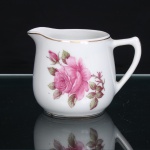 PORCELANA RAMI, Jundiaí  São Paulo (fundada em 1930). Leiteira em porcelana nacional, de esmaltação branca, com decoração floral em estampagem policromada, predominando tonalidades rosa e verde. Corpo bojudo, assente sobre base circular; embocadura de contorno sinuoso, prolongada em bico vertedor ondulado e revirado para fora; alça lateral arqueada e estilizada. Bordo e base percorridos por frisos em douradura. Marca de manufatura PORCELANA RAMI na base.  Medidas: Alt.: 8,5 x Comp.: 12 x Larg.: 9cm.