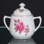 PORCELANA RAMI, Jundiaí  São Paulo (fundada em 1930). Açucareiro em porcelana nacional, de esmaltação branca, com decoração floral em estampagem policromada, predominando tonalidades rosa e verde. Corpo bojudo, assente sobre base circular, provido de duas alças laterais arqueadas e simétricas; tampa abobadada com pomo torneado. Ornamentação complementada por frisos em douradura contornando a abertura, base, tampa e pomo. Marca de manufatura PORCELANA RAMI na base. Medidas: Alt.: 14 x Comp.: 15 x Larg.: 10cm.
