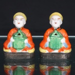 Par de queimadores de incenso em porcelana japonesa, período da ocupação c.19451952. Par de figuras em porcelana moldada e policromada, representando personagens orientais sentados, trajando vestes em vermelho-alaranjado com motivos circulares em negro e toucados amarelos. Cada personagem sustenta diante do torso recipiente ritual em verde, provido de abertura triangular e vazados superiores destinados à dispersão da fumaça, configurando queimadores de incenso. Bases retangulares moldadas com friso geométrico em relevo e acabamento escuro. Reverso apresenta ampla abertura para colocação do incenso. Base com carimbo MADE IN OCCUPIED JAPAN, inscrição empregada em artigos japoneses destinados à exportação durante a ocupação aliada do Japão, permitindo situar sua produção entre 1945 e 1952. Medidas: Alt.: 8,5 x Comp.: 6,5 x Larg.: 4cm.