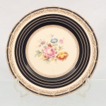 Prato em faiança inglesa Ridgways, manufatura de Shelton, Staffordshire, estilo Vitoriano com reedição de padrão clássico, circa início do século XX. Centro apresenta policromia transferida por decalque e finalizada à mão com buquê floral composto por rosa, dália e ramificações fitomórficas, emoldurado por cercadura geométrica cruciforme. Aba larga delimitada por faixas circulares em azul-cobalto sob o vidrado, intercaladas por filetes dourados e cercadura perimetral com guirlandas de folhas de louro sobre fundo marfim. Verso exibe craquelê natural do esmalte e ostenta a marca do fabricante estampada em tom dourado com as inscrições "Ridgways England / Shelton England / Estd 1792". Medida: Diam.: