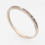 JOIA. Anel confeccionado metal prateado, de aro estreito, guarnecido na face superior por sequência de pequenas pedras de lapidação circular, em diferentes tonalidades: azul, rosa, violeta, amarelo e verde, dispostas alternadamente em cravação por garras. Medida: Diam.: 2 cm. ; Peso: 0.8 gramas.