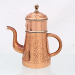 Cafeteira com filtro em metal acobreado. Corpo obcônico com alça lateral tubular e bico elevado de perfil curvilíneo. Parte superior constituída por compartimento cilíndrico para café, identificado por plaqueta em latão com inscrição COFFEE, encimado por tampa abaulada com pomo torneado. Interior dotado de filtro metálico removível perfurado, destinado à preparação da bebida por percolação. Elementos de união e guarnições em metal. Superfície com oxidação e alterações de pátina decorrentes do uso. Medidas: Bule: Alt.: 23,5 x Comp.: 22 x Larg.: 11,5cm; Medidas filtro: Alt.: 10 x Diam.: 9cm.