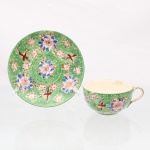 Xícara com pires em porcelana japonesa. Corpo moldado em porcelana, com esmaltação verde e composição policroma de motivos florais e aves em voo, executada em rosa, azul, vermelho, amarelo, branco e preto. Campo preenchido por pontilhado branco em relevo; alça e bordas com douração. Pires circular com ornamentação correspondente, distribuída em arranjo radial. Interior da xícara em esmalte marfim, apresentando craquelê. Marca em azul sob a base, com emblema de manufatura e inscrição "Made in Japan". Japão, primeira metade do século XX.Medidas xícara: Alt.: 4,5 x Comp.: 10 x Larg.: 8,5 cm; Pires: Diam.: 13 cm. Interior da xícara apresneta manchas do tempo.