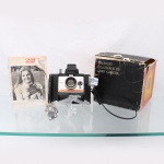 Câmera fotográfica instantânea Polaroid Colorpack 80 Land Camera, Estados Unidos, década de 1970. Corpo em material sintético preto, painel frontal metálico, visor óptico elevado, objetiva com regulagem de distância e controle de exposição. Acompanha dois flashes descartáveis tipo flashcube Atlas, Made in Great Britain, alça, manual impresso e caixa original Polaroid Colorpack 80 Land Camera. Na parte posterior, conserva placa de instruções multilíngue para utilização do acessório Polaroid 195X em condições de baixa temperatura. Conjunto apresenta marcas de uso, oxidação em componentes metálicos e desgastes na embalagem. Não foi testado, sem garantias de funcionamento. Medidas: Alt.: 14 x Comp.: 15 x Larg.: 14cm.