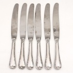 MERIDIONAL EPNS 100. Elegante conjunto de facas grandes confeccionadas em metal espessurado à prata(EPNS 100), cabo violinado com filetes longitudinais em baixo-relevo e terminação ornamentada por composição de concheados, volutas, flores e folhagens em relevo. Lâmina em aço inox. Marca da manufatura gravada na lâmina, e identificação EPNS 100 puncionada no cabo. Composto de seis(06) unidades. Medidas: Comp.: 23,5 cm.