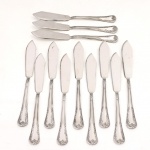 MERIDIONAL EPNS 100. Elegante conjunto de facas para peixe confeccionadas em metal espessurado à prata(EPNS 100), cabo violinado com filetes longitudinais em baixo-relevo e terminação ornamentada por composição de concheados, volutas, flores e folhagens em relevo. Marca da manufatura puncionada no verso. Composto de doze(12) unidades. Medida: Comp.: 20 cm.