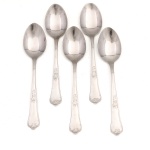 HERCULES INOX. Modelo Classique. Conjunto composto por cinco(05) colheres para sobremesa confeccionadas em aço inoxidável, datável do período circa 1960-1970. Executados ao estilo francês do período Luís XV, apresentam cabos de perfil sinuoso e terminação espatulada, enriquecidos por ornamentação seriada em relevo que conjuga motivos de volutas, rocalhas e filetes perimetrais. O reverso das hastes exibe a marca em baixo-relevo "HERCULES INOX". Medida: Comp.: 17 cm.