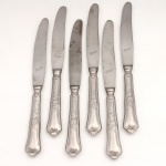 HERCULES INOX. Modelo Classique. Conjunto composto por seis(06) facas grandes confeccionadas em aço inoxidável, datável do período circa 1960-1970. Executados ao estilo francês do período Luís XV, apresentam cabos de perfil sinuoso e terminação espatulada, enriquecidos por ornamentação seriada em relevo que conjuga motivos de volutas, rocalhas e filetes perimetrais. Lâminas exibem gume com acabamento serrilhado de fábrica e faces frontais com gravação em matriz ácida "Hercules AÇO INOX", integrada à efígie do fabricante sob o selo de têmpera especial "GELODUR". O reverso exibe a marca em baixo-relevo "HERCULES INOX". Medida: Comp.: 24,5 cm.