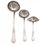 HERCULES INOX. Modelo Classique. Três(03) peças para servico: Uma(01) concha para sopa, uma(01) concha para feijão e uma(01) concha para molho confeccionadas em aço inoxidável, datável do período circa 1960-1970. Executados ao estilo francês do período Luís XV, apresentam cabos de perfil sinuoso e terminação espatulada, enriquecidos por ornamentação seriada em relevo que conjuga motivos de volutas, rocalhas e filetes perimetrais. Lâmina cega com ponta proeminente e sem corte. O reverso das hastes exibe a marca em baixo-relevo "HERCULES INOX" flanqueada pela especificação da liga metálica de alta resistência "18-8". Medidas: Comp.: 17 x Larg.: 8,5 cm; Comp.: 21 x Larg.: 7,5 cm; Comp.: 29 x Larg.: 9 cm.