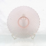 Prato de servir em vidro prensado, translúcido, tonalidade rosa, superfície integralmente moldada com padrão geométrico de losangos, centro rebaixado delimitado por anéis concêntricos e decoração radial. Bordo ondulado, acompanhando a sucessão de facetas.Medidas: Diam.: 33cm.