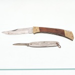 Dois(02) canivetes de bolso: a) Utilitário de caça ou sapataria com mecanismo de travamento por mola dorsal(lockback), provido de lâmina de aço carbono de perfil clip point, cabos revestidos por talas de madeira fixadas por rebites de latão e virolas polidas no mesmo metal na extremidade oposta. Medidas: Aberto: Comp.: 18 x Larg.: 3 cm; Fechado:  Comp.: 10,5 x Larg.: 3cm; b) Canivete publicitário e comemorativo duplo, manufaturado em metal niquelado pela firma Uhlitzsch y Cía., sediada na rua Cramer 1376, Buenos Aires, Argentina(circa 1930-1940). Suas cachas metálicas ostentam inscrições em alto-relevo da marca "Wiltzsch 'Miche' Chocolata" e a indicação geográfica da empresa, contendo lâmina menor de perfil reto e argola de suspensão integrada na extremidade posterior. Medidas: Aberto: Comp.: 13 x Larg.: 1,5 cm; Fechado: Comp.: 7 x Larg.: 1,5 cm.