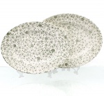 Duas(02) travessas em faiança nacional, manufatura Nadir Figueiredo. Formato oval, esmaltação branca, decorada por estampa de tonalidade verde, composta por pequenos motivos florais e folhagens distribuídos de maneira contínua pela superfície. No reverso, marca "Pottery - Decoration Hand Engraved  Printed Underglaze  Made in Brazil", correspondente à manufatura Nadir Figueiredo, com decoração impressa sob o esmalte. Medidas maior: Alt.: 2,5 x Comp.: 28 x Larg.: 21,5 cm; Medidas menor: Alt.: 2,5 x Comp.: 26,5 x Larg.: 20 cm.