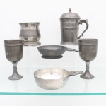 Conjunto de seis(06) peças em estanho(pewter), composto por caneca com tampa articulada e asa em voluta, par de cálices de haste curta, copo de corpo abaulado, pequena escudela com pega lateral e dois porringes com cabo vazado. Superfícies lisas ou molduradas por frisos concêntricos, com diferentes marcas de manufatura e contraste. Medidas caneca: Alt.: 16 x Comp.: 14 x Larg.: 9,5 cm;Medidas taça: Alt.: 15,5 x Diam.: 8cm; Medidas copo: Alt.: 10 x Diam.: 10cm. Medidas: Alt.: 4,5 x Comp.: 7,5 x Larg.: 12,5cm. Medidas: Alt.: 4 x Comp.: 17 x Larg.: 12cm.