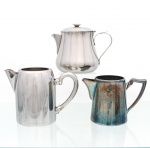 Três (03) peças para serviço de café em aço inoxidável, composto por cafeteira com tampa articulada e duas leiteiras de diferentes modelos, todas com corpos de superfície lisa, bicos vertedores e alças laterais. Uma das peças apresenta marca gravada "Fracalanza  Aço Inoxidável" na base. Uma leiteira necessita polimento e/ou refazer banho de prata. Medidas maior: Alt.: 12 x Comp.: 17 x Larg.: 9 cm; Medidas menor: Alt.: 10 x Comp.: 15 x Larg.: 8,5 cm.