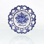 Prato decorativo em faiança portuguesa - Alcobaça, Portugal. Prato circular de parede moldada, com aba vazada e recortada em motivos florais. Decoração policroma executada à mão em azul-cobalto sobre fundo branco, composta por arranjo floral central e ornatos florais distribuídos pela aba. Ao centro, inscrição manuscrita "Portugal". No reverso, marca de manufatura parcialmente preservada, com indicação "Alcobaça - Portugal". Medida: Diam.: 20,5 cm.
