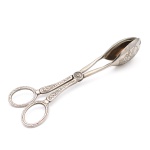 Pinça para serviço de salada em metal prateado, utensílio articulado em formato de tesoura, com empunhaduras anelares e braços ornamentados por motivos fitomórficos em relevo. Extremidades constituídas por duas conchas ovais côncavas, gravadas com composição de frutos e folhagens. Articulação central com inscrição parcialmente legível. Medida: Comp.: 22cm.