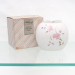 Vaso em porcelana inglesa fine bone china, manufatura Royal Grafton, Inglaterra. Corpo de formato globular achatado, em porcelana branca, com abertura superior recortada em dupla concavidade. Decoração floral policroma com flores em tonalidades rosa, folhagens verdes e pequenos elementos em azul e ocre. Acompanha caixa original da linha "The Marlborough Collection - English Fine Bone China by Royal Grafton". Medidas: Alt.: 12 x Comp.: 13 x Larg.: 10cm.