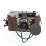 Câmera fotográfica analógica japonesa Taron Taron U, para filme 35 mm, com visor telemétrico. Equipada com objetiva Taronar F.C. 45 mm f/2.8, obturador Citizen-P, controles de abertura, velocidade e distância dispostos no conjunto óptico. Corpo metálico com revestimento preto, estojo parcial em couro, alça e tampa frontal da objetiva. Japão, circa década de 1960. Estado de conservação conforme fotografias, não foi testada, sem garantias de funcionamento. Medidas: Alt.: 9,5 x Comp.: 14,5 x Larg.: 8cm.