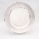 EBERLE. Elegante sousplat confeccionado em metal espessurado a prata, formato circular de centro ligeiramente rebaixado, aba larga e lisa. Sem uso. Acondicionado em embalagem original(no estado). Marca da manufatura no verso. Medida: Diam.: 30,5 cm.