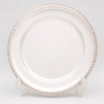 Bandeja confeccionada em metal espessurado à prata, formato circular, centro liso ligeiramente rebaixado, borda ricamente relevada com motivos fitomórficos estilizados e fundo texturizado em pontilhado, arrematada na borda extrema por friso perlado. Necessita apenas polimento no verso. Medida: Diam.: