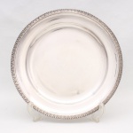 Bandeja confeccionada em metal espessurado à prata, formato circular, centro liso ligeiramente rebaixado, borda ricamente relevada com motivos fitomórficos estilizados e fundo texturizado em pontilhado, arrematada na borda extrema por friso perlado. Necessita apenas polimento no verso. Medida: Diam.: