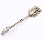 Pinça para servir bolo confeccionada em metal prateado. Utensílio articulado em forma de tesoura, com aros ovais, hastes molduradas por frisos e terminais de preensão assimétricos: um vazado e outro constituído por placa retangular de contorno recortado. Superfícies ornamentadas por gravação de volutas, folhagens e motivos fitomórficos. Articulação central com inscrição "SILVERPLATED". Medida: Comp.: 22cm.