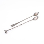Duas(02) colheres longas para coquetel em metal prateado, manufatura Eberle, fabricação nacional. Duas peças de bar, ambas com concha oval e hastes alongadas. Um exemplar apresenta cabo parcialmente torsado e terminal espatulado; o outro possui haste facetada e extremidade rematada por disco estriado, destinado à maceração de ingredientes, funcionando como pilão para coquetelaria. Conservam marca "EBERLE" e punções numéricos junto à junção da concha. A Metalúrgica Abramo Eberle, fundada em Caxias do Sul em 1896, iniciou a fabricação de talheres, cutelaria e utensílios de mesa em 1918. Medidas: Comp.: 25,5cm; Comp.: 25cm.