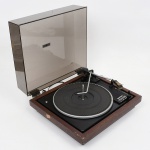 Toca-discos automático, modelo Gradiente Garrard S-95, montado em base retangular em madeira, com tampa articulada em acrílico fumê. Plataforma circular com prato metálico e tapete emborrachado, eixo central para acomodação de discos e braço de leitura articulado com cápsula fonocaptora. Sistema seletor de velocidades (33, 45 e 78 rpm) e chave de operação com funções off, manual e automatic. Painel com identificação do modelo e marca.Parte posterior com saídas de áudio (left/right), chave seletora de voltagem (110/220 V) e cabo de alimentação fixo. Inscrição na base: Gradiente Amazônia S.A., Indústria Brasileira, produzido na Zona Franca de Manaus. Não foi testado, sem garantias de funcionamento. Estado conforme fotografias. Medidas: Alt. 17 x Comp.: 37 x Larg.: 23 cm.