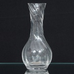 Vaso executado em vidro translúcido, corpo globular afilado em direção ao colo alongado, estruturado com torção helicoidal obtida por modelagem base espessada e boca circular simétrica, produzidas no mesmo processo de sopro e conformação. Medidas: Alt.: 13 x Diam.: 6 cm.