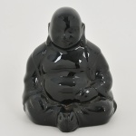 Estatueta executada em cerâmica vitrificada, esmaltagem de tonalidade preta, representando Buda ou Hotei sentado em posição de meditação. Med.: Alt. 17 x Comp. 14 x Larg. 13 cm.
