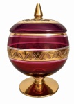VENEZA - Bombonière em cristal artístico veneziano na tonalidade rubi, com tampa e base em vibrante ouro, rica decoração em frisos lapidados e faixas douradas. Peça de elegante acabamento, ideal para compor ambientes clássicos ou coleções de cristais. Circa 1900. Desgaste do tempo. Medida: 23 cm de altura.