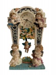 Relógio de mesa em resina, decorado com figuras de querubins, flores em relevo e anjo pendente, movimento a quartzo. Apresenta sinais naturais de uso e conservação compatíveis com o tempo. Não testado. Medidas: 21  13