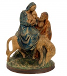 Grupo escultórico religioso representando a Fuga para o Egito, com a Virgem Maria ao colo do Menino Jesus sobre jumento, acompanhada por São José. Escultura em composição moldada gesso com policromia em tons terrosos e azul, sobre base oval. Apresenta marcas compatíveis com o tempo. Medidas: 24 cm de altura x 21 cm.