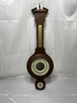 Barômetro aneroide de parede vintage com estrutura em madeira nobre, integrando termômetro capilar superior e higrômetro inferior, com mostradores ornamentados em espanhol e acabamento clássico. Medindo 16,5cm de mostruário x 67cm de comprimento. Faltando o vidro.