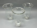 Trio de antigas cúpulas ou mangas para castiçal, serpentina ou lustre, confeccionadas em demi cristal translúcido liso com sutil tonalidade esverdeada. Apresentam gracioso formato bojudo com gargalo estreitado e boca superior em formato de tulipa com borda ondulada em babado. Medidas: 18x10x4,5 cm. Apresentam marcas do tempo, de uso e bicados.