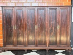 MOBILIÁRIO - Magnífico guarda-roupa / armário de grande porte em madeira nobre (Jacarandá) com belíssimo trabalhado de veios aparentes. Estrutura imponente com seis portas, elegantes puxadores e espelhos de fechadura em metal dourado com lavor clássico, além de detalhes entalhados nas colunas laterais. O interior é totalmente compartimentado, contando com nichos espaçosos para cabides, prateleiras e módulos de gaveteiros internos embutidos. Med. 195x298x63 cm. <br><br>Móveis Usados - Lote de móvel antigo e usado, podendo apresentar marcas de uso e desgaste natural do tempo. Há possibilidade de danos ocultos e ou outras imperfeições. Não há garantia ou possibilidade de devolução após a aquisição. Recomenda-se inspeção prévia.
