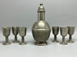 PEWTER - Elegante conjunto em pewter, composto por uma garrafa de corpo bojudo com tampa (maior, com 21 cm de altura) e um conjunto de 6 cálices coordenados (com 8,5 cm de altura cada). Marcas do tempo e de uso. Leves amassados.