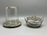 DEMI CRISTAL - Charmoso conjunto composto por duas peças em demi cristal com acabamentos e suportes em metal espessurado a prata, incluindo um recipiente cilíndrico alto com tampa e prato de base e um açucareiro com suporte, tampa e colher dedicada. Med. maior 16 cm e 8 cm. Marcas do tempo e de uso.
