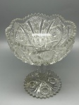 CRISTAL - Fruteira alta, decorada com rica lapidação geométrica com motivos de estrelas e losangos em relevo, borda serrilhada trabalhada e base com pé elegante e estruturado. Med. 19x16 cm. Marcas do tempo e de uso. Leves bicados.