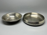 INOX - Conjunto utilitário em aço inoxidável composto por duas peças de formatos arredondados: uma bacia funda com aba larga e uma tigela rasa de borda lisa e corpo bojudo. Med. 6x27 cm e 6x29 cm. Marcas do tempo e de uso.
