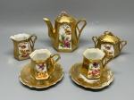 PORCELANA - Requintado conjunto miniatura do tipo tête-à-tête em porcelana com rica aplicação de douração brilhante por toda a superfície externa e reservas decoradas à mão com pinturas policromadas de flores e ramagens delicadas, apresentando formato geométrico hexagonal com bordas onduladas e alças angulares trabalhadas, sendo composto por um bule com tampa e puxador vazado, um açucareiro com tampa correspondente, uma leiteira de corpo cônico e bico vertedor recortado, duas xícaras de café com formatos poligonais e dois pires com acabamento dourado texturizado. Maior 11 cm e menor 5,5 cm. Desgastes e marcas do tempo e de uso.