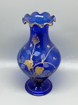 DEMI CRISTAL - Vaso floreira em demi cristal na tonalidade azul cobalto, com corpo bojudo elegante, base circular estável e borda superior ondulada. A peça é ricamente adornada com pintura manual em relevo dourado e esmalte branco, destacando motivos florais estilizados e ramagens delicadas que se estendem por todo o corpo. O acabamento conta com filetes dourados aplicados na borda do bocal e no contorno da base. Med. 25x9 cm. Marcas do tempo e de uso.