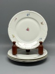 PORCELANA - Charmoso conjunto composto por 4 pratos rasos em porcelana branca de fabricação fina, com abas de borda ondulada adornadas por delicado relevo em padrão vegetal contínuo. O espelho de cada peça apresenta um elegante bouquet floral policromado ao centro, complementado por pequenos raminhos de flores coloridas dispersos pela aba. O verso de cada prato exibe a marca de fabricação da antiga Checoslováquia com o emblema de águia e monograma "MZ", além de marcações numéricas em relevo e tinta verde. Dia. 19,5 cm. Marcas do tempo e de uso.