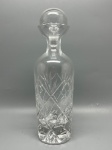 CRISTAL - Elegante licoreira em cristal lapidado transparente, apresentando corpo cilíndrico trabalhado com motivos geométricos em relevo de losangos e estrelas, base espessa com lapidação radial e gargalo estreito com gola alargada, acompanhada de tampa esférica lapidada ajustada. Medindo 29 cm de altura, a peça encontra-se em excelente estado de conservação, com desgastes naturais do tempo e marcas de uso.