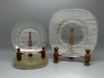 DEMI CRISTAL - Conjunto de oito pratos em vidro transparente com textura ondulada em relevo, formato quadrado de cantos arredondados, composto por 4 pratos de servir medindo 28x28 cm e 4 pratos de sobremesa medindo 18x18 cm, apresentando desgastes naturais do tempo e marcas de uso.